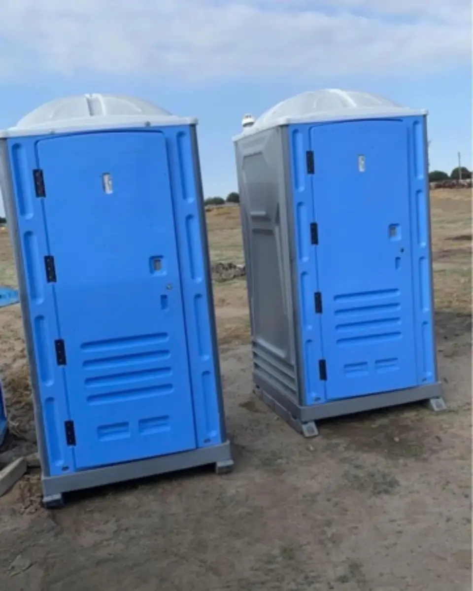 Two blue porta potties on a dirt jobsite lot