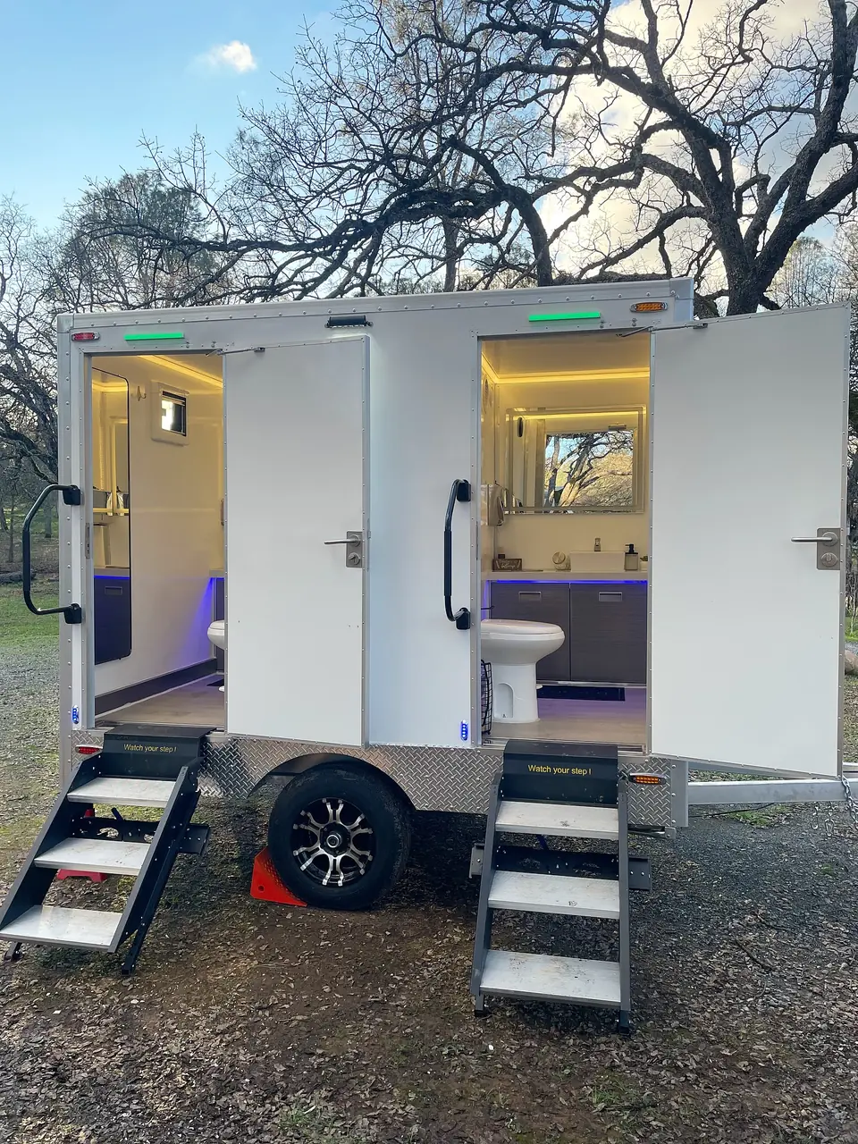 Two-stall restroom trailer with its interior lights on at dusk